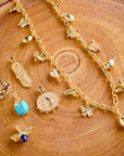 Stylized shot on a wood slice of pendants including 14k protect cutout coin, joy camellia dogtag, lucky ladybug coin, turquoise scarab, and sisters bee. Also features the joy garden party charm necklace.