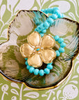 Stylized shot of the joy camellia pendant and the turquoise beaded necklace in flower dish on a green and white floral patterned background