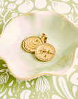 Stylized shot showing the front and back of the lucky petite embellished coin in a light green ceramic dish