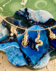 Stylized shot of solid gold critters including the chickadee, grasshopper, snake, and ladybug on the omega wire chain resting on a blue agate slice