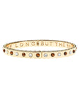 Thin gold hinge cuff features alternating cabochons of Mother of Pearl and tiger's eye stones on the outside and the phrase "the days are long but the years are short" inscribed on the inside.