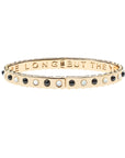 Thin gold hinge cuff features onyx and mother of pearl stones on the outside and the phrase "the days are long but the years are short" inscribed on the inside