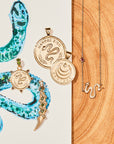 Stylized laydown image of three gold coin pendants and two snake pieces with sketch of design