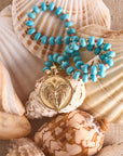 Stylized shot of the strong love of the sea coin pendant on the turquoise and coral beaded on a pile of seashells