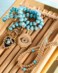 Stylized shot of the turquoise and coral beaded necklace, turquoise and gold bead double wrap, protect with an open eye pendant and protect queen of hearts pendant