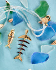 Stylized shot of strong fishbone pendant, strong rainbow fish pendant, double wrap in aquamarine on turquoise background with seaglass pieces