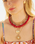 Model wearing various sun pendants, gold chains, and coral beaded necklace