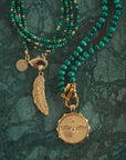Stylized shot of the protect eagle coin, lucky feather pendant, malachite and gold double wrap necklace, and malachite beaded necklace.