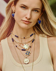 Model wearing lapis set in stone earrings as well as various gold and lapis pendants and chains
