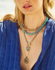 Model wearing various gold chains and beaded necklaces with evil eye pendants