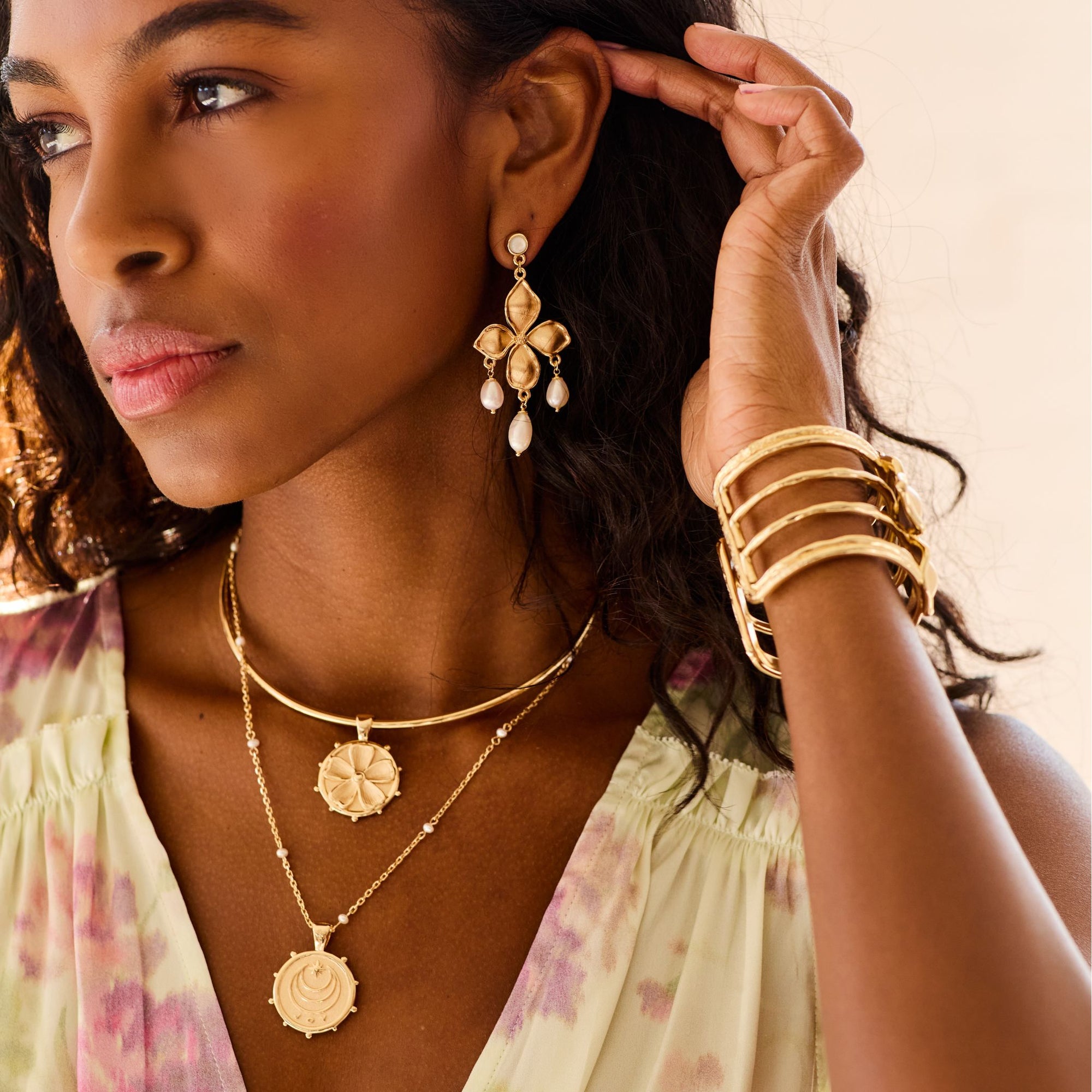 Model wearing gold dogwood cuff, dogwood pearl drops, and perwinkle coin