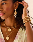 Model wearing gold dogwood cuff, dogwood pearl drops, and perwinkle coin