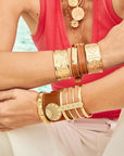 Model wearing assorted gold cuffs and leather bracelets