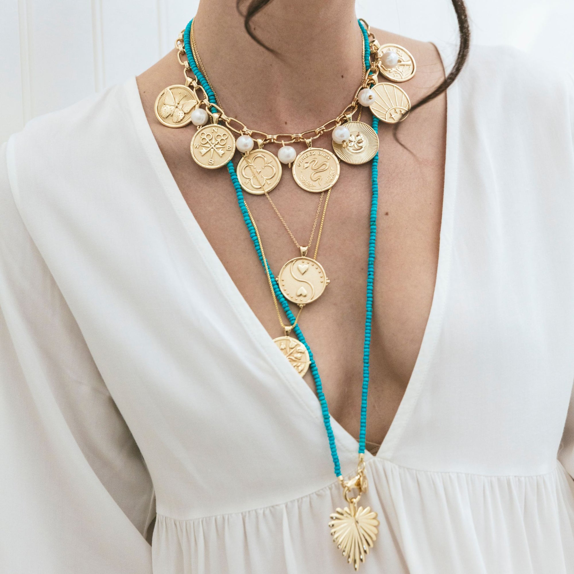 Model wearing various gold coins and long turquoise beaded necklace