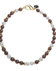 Beaded necklace featuring round wood and pearl beads with flat gold peads interspersed. Necklace features oversized gold lobster clasp