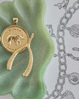 Stylized shot of bonne chance elephant coin and lucky pave wishbone in green dish on a sketch of jewelry