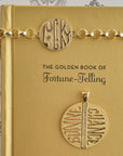 Stylized show of jumbo bonne chance coin and bonne chance coin bracelet on a gold book