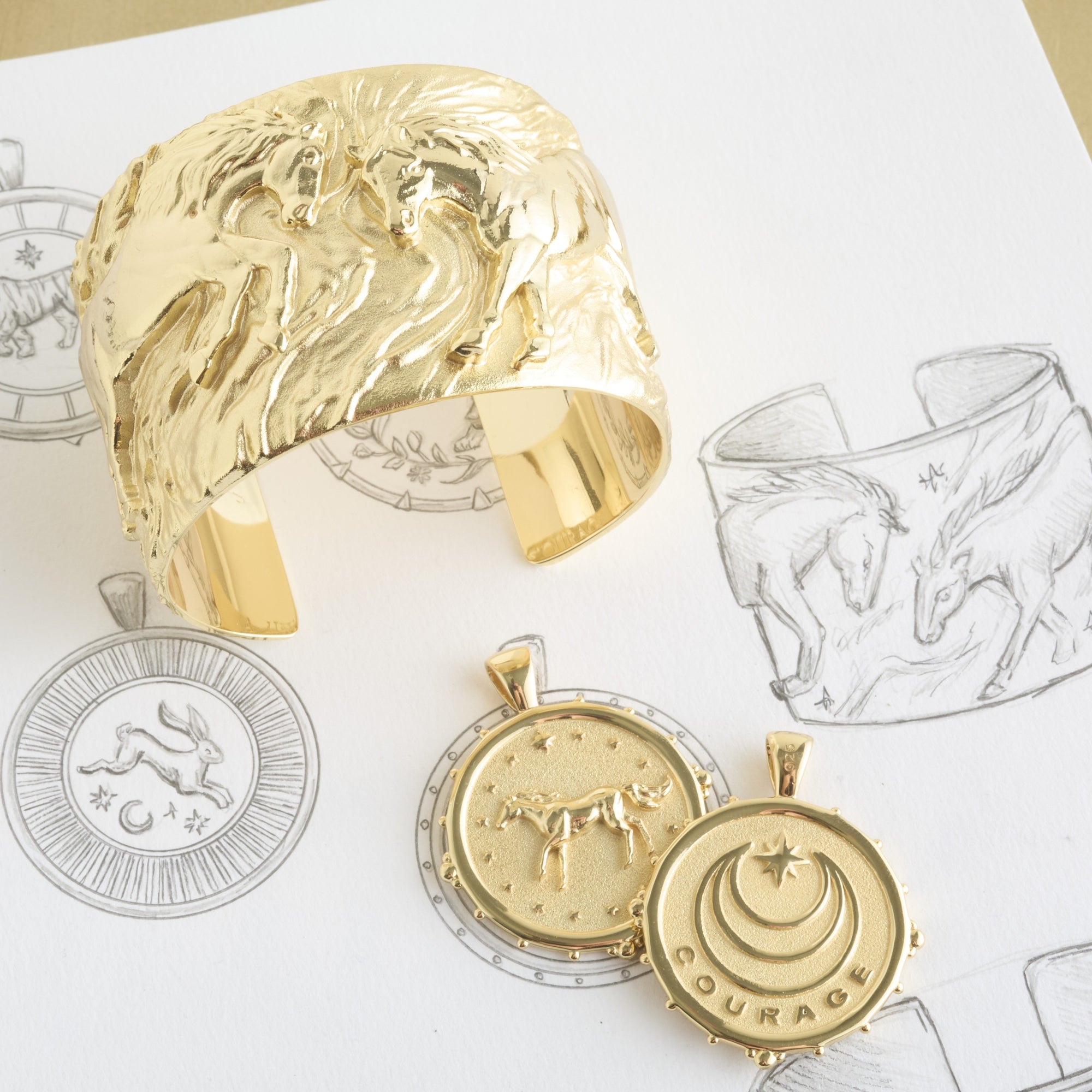 Stylized shot of horse cuff and front & back of horse coin on top of page of jewelry sketches