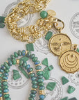 Stylized shot of front and back of eagle coin, gold chain, beaded chain, and malachite pieces on a page of sketches of the coins