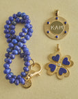 Stylized shot of beaded lapis chain and engraved forever around the sun pendant, and lapis clover pendant