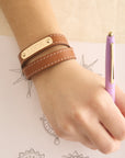 Model wearing brown leather double wrap bracelet with sample engraving of the word LUCK