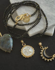 Stylized shot of labradorite heart pendant, mother of pearl moon face pendant, and onyx crescent moon pendant with black beaded necklace