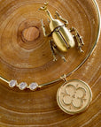 Stylized shot of the embellished neck cuff with the love coin on a piece of wood with a gold beetle figurine