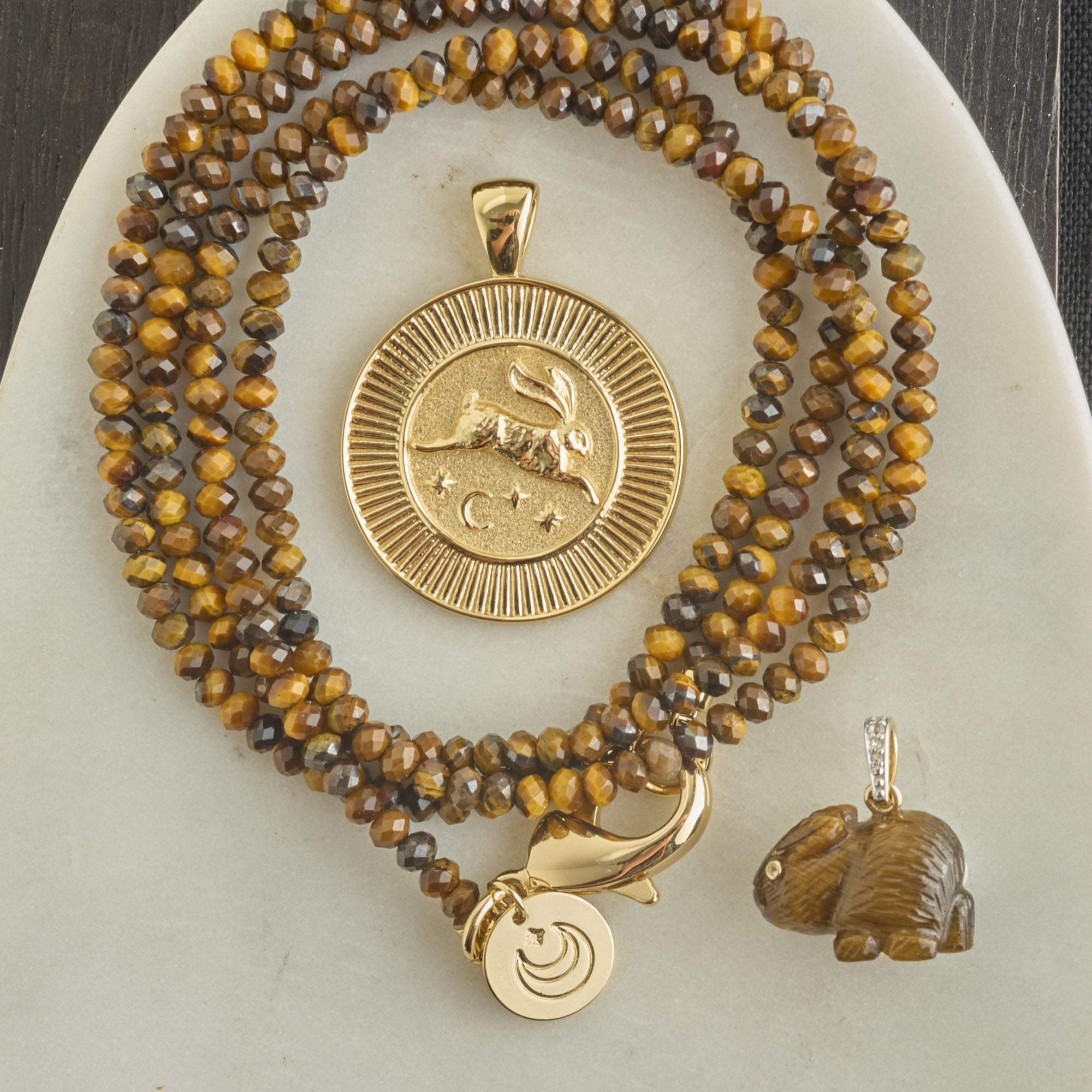 Stylized shot of gold rabbit coin, tigers eye beaded chain, and carved tigers eye rabbit