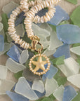 Stylized shot of starfish cutout coin on mother of pearl beaded necklace laying on a pile of sea glass