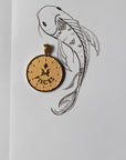 Gold original Pisces coin pendant next to a drawing of a fish
