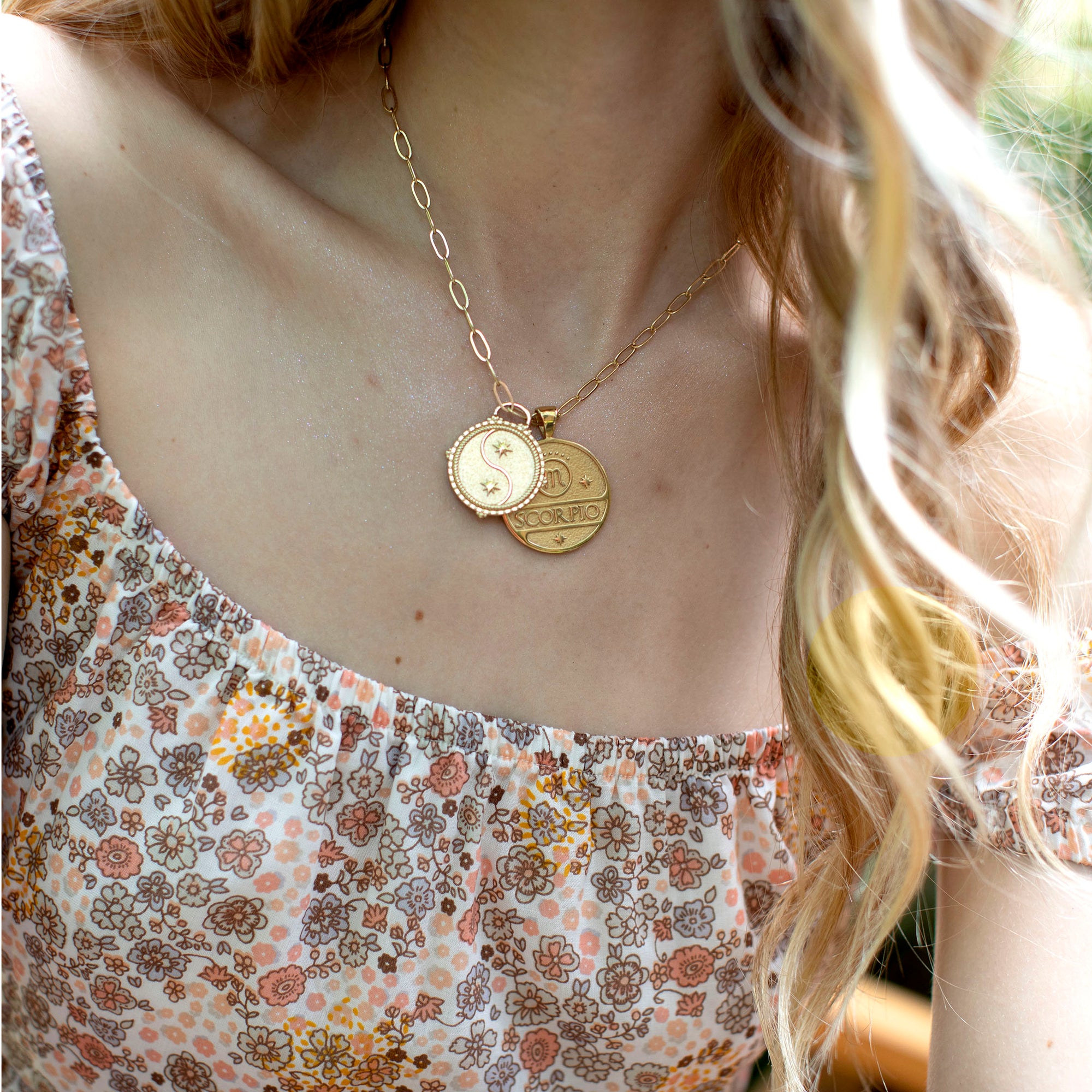 Model wearing the gold original size Scorpio pendant and small Gemini pendant on the same chain