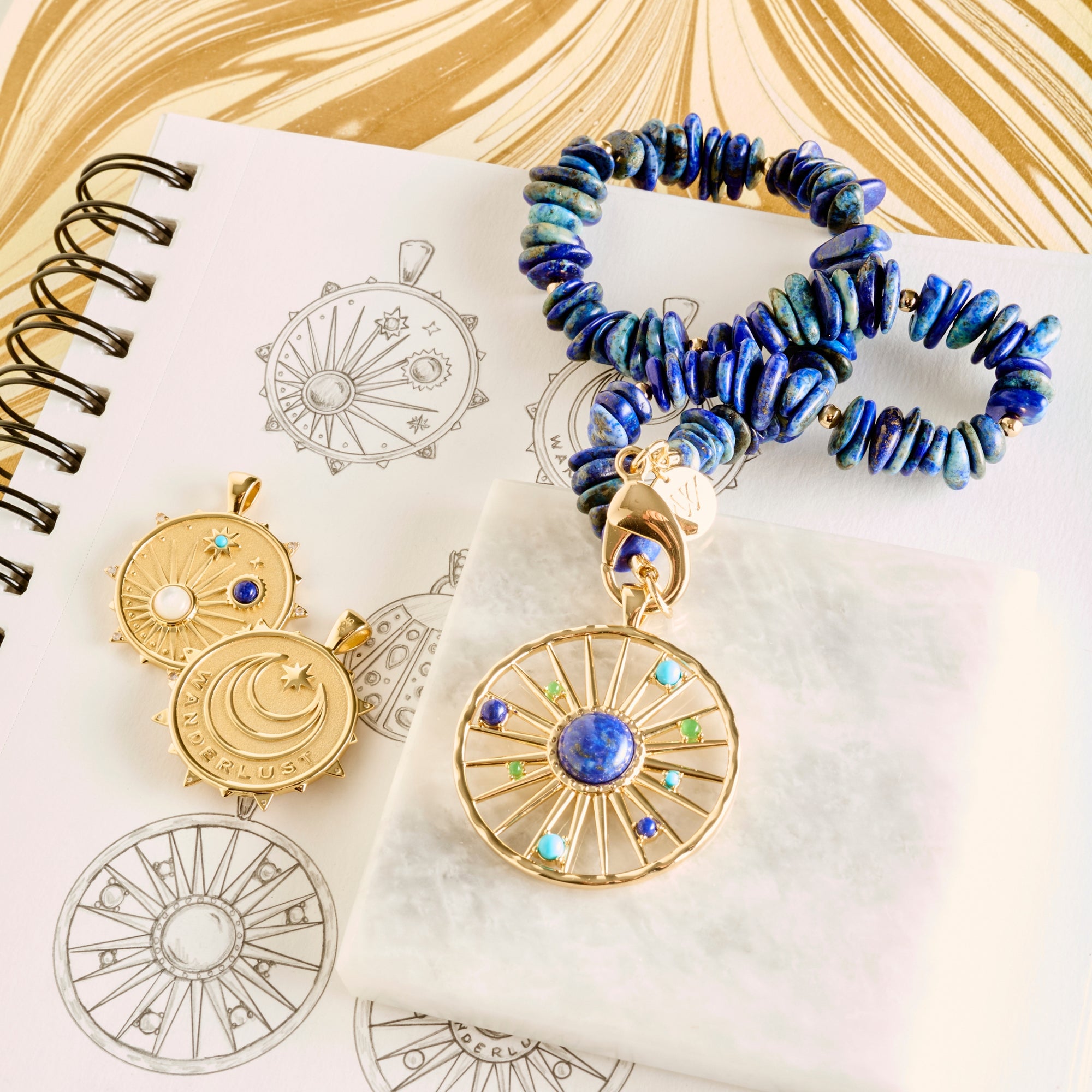 Stylized shot of wanderlust coins and lapis beaded necklace on sketches of the designs