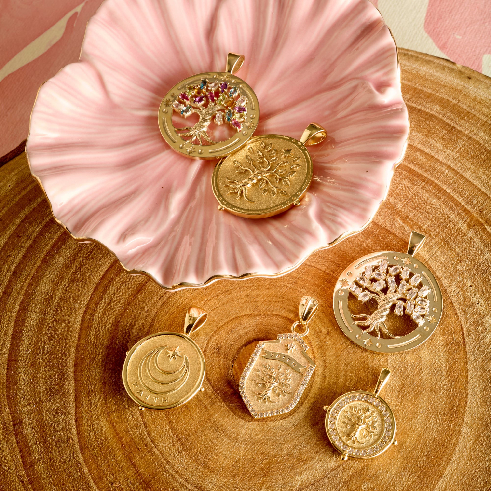 Stylized shot of pendants from the faith collection on a slice of wood and in a pink ceramic flower dish