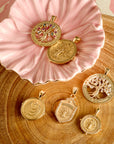Stylized shot of pendants from the faith collection on a slice of wood and in a pink ceramic flower dish