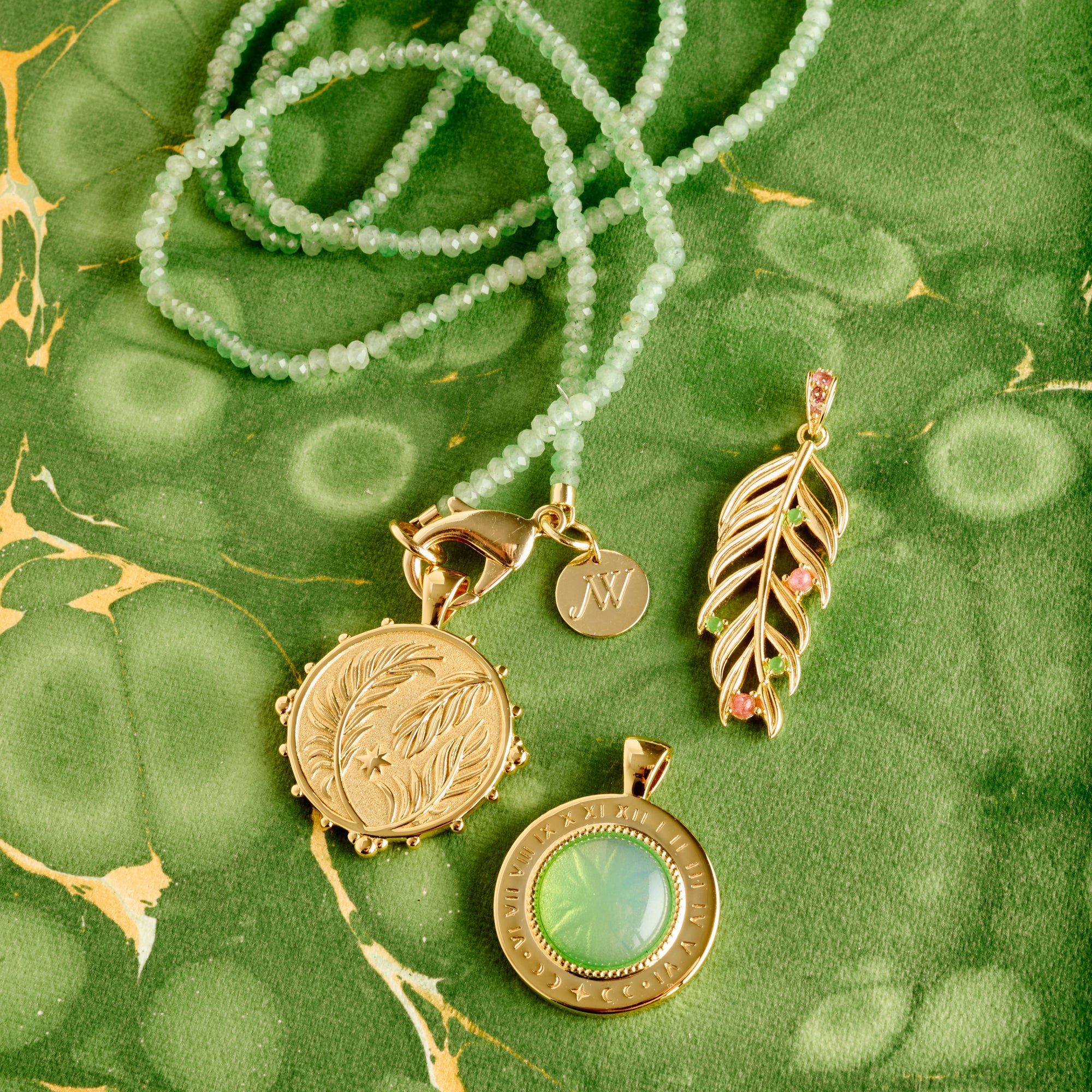 Stylized shot on marbled green background of the wanderlust palm coin, palm leaf, forever under the sun pendant, and double wrap in green jade 