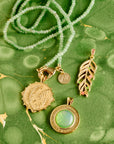 Stylized shot on marbled green background of the wanderlust palm coin, palm leaf, forever under the sun pendant, and double wrap in green jade 