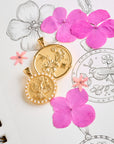 Stylized shot of the joy camellia coin and joy chickadee embellished coin on a page of sketches of the designs and pink flowers