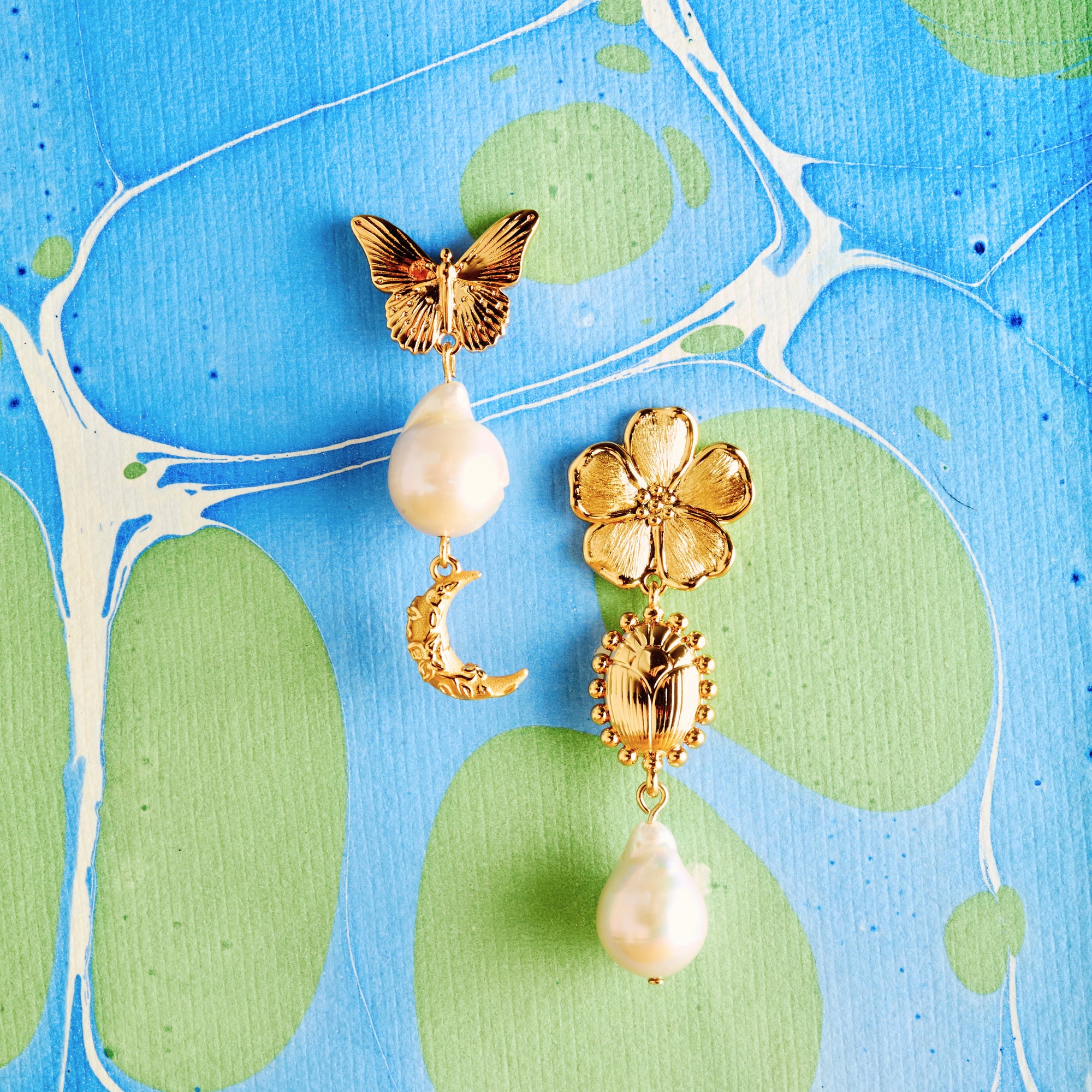 Stylized shot of the joy tea party earrings on marbled blue and green paper background
