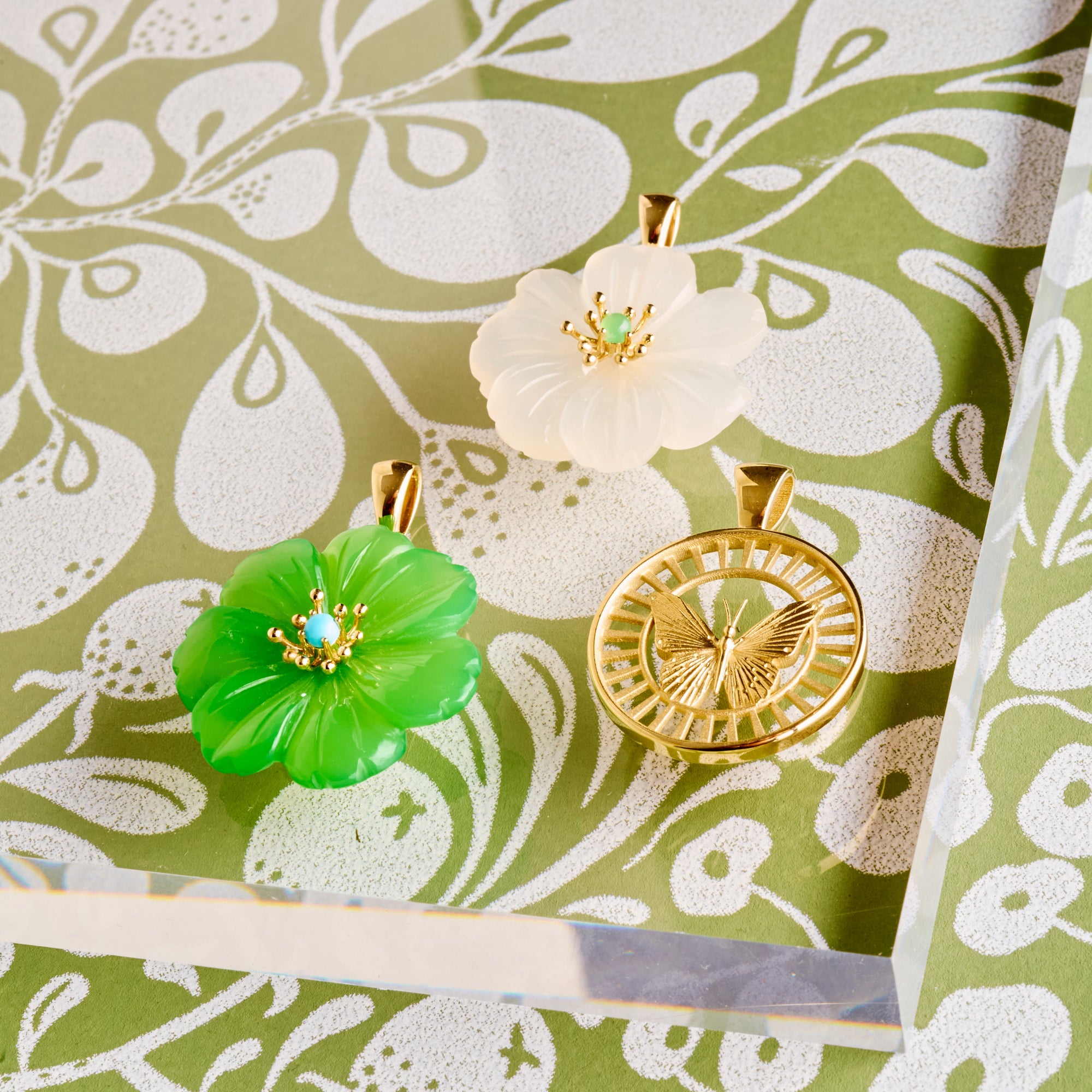 Stylized shot of the moonstone and chrysophrase carved camellias and the 14k free cutout coin on greenand white floral patterned background