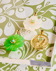 Stylized shot of the moonstone and chrysophrase carved camellias and the 14k free cutout coin on greenand white floral patterned background
