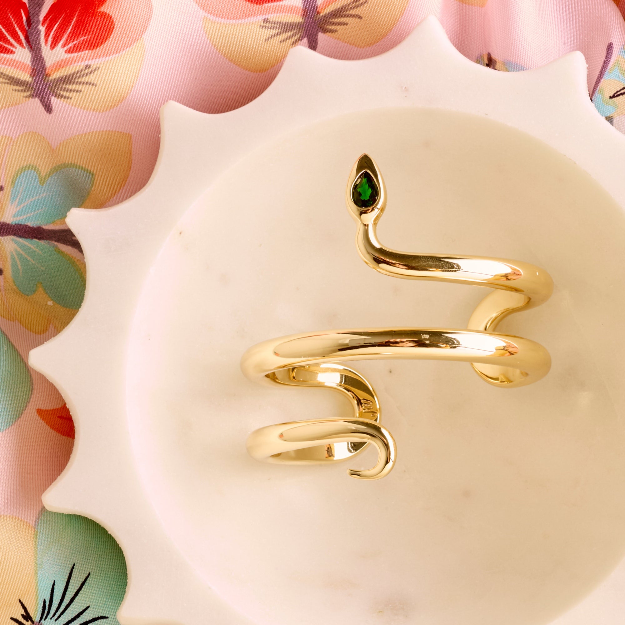 Stylized shot of the protect snake cuff in a marble dish sitting on floral fabric