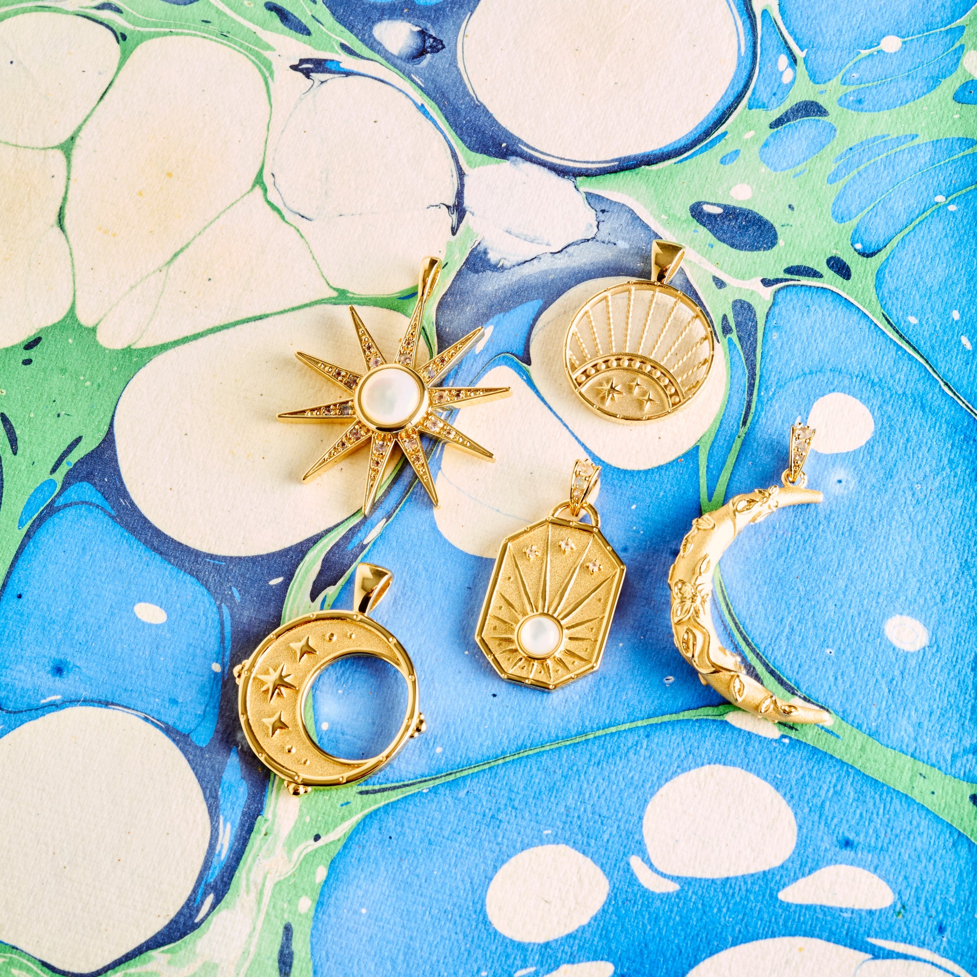 Stylized shot of moon, star, and sun pendants on blue and green marbled paper