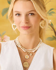 Model wearing the love in the sun earrings in mother of pearl, double wrap opal necklace with love petite embellished coin, and joy original coin on an adjustable snake chain