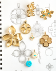 Stylized shot of gold flower pendants and earrings with sketches of the designs