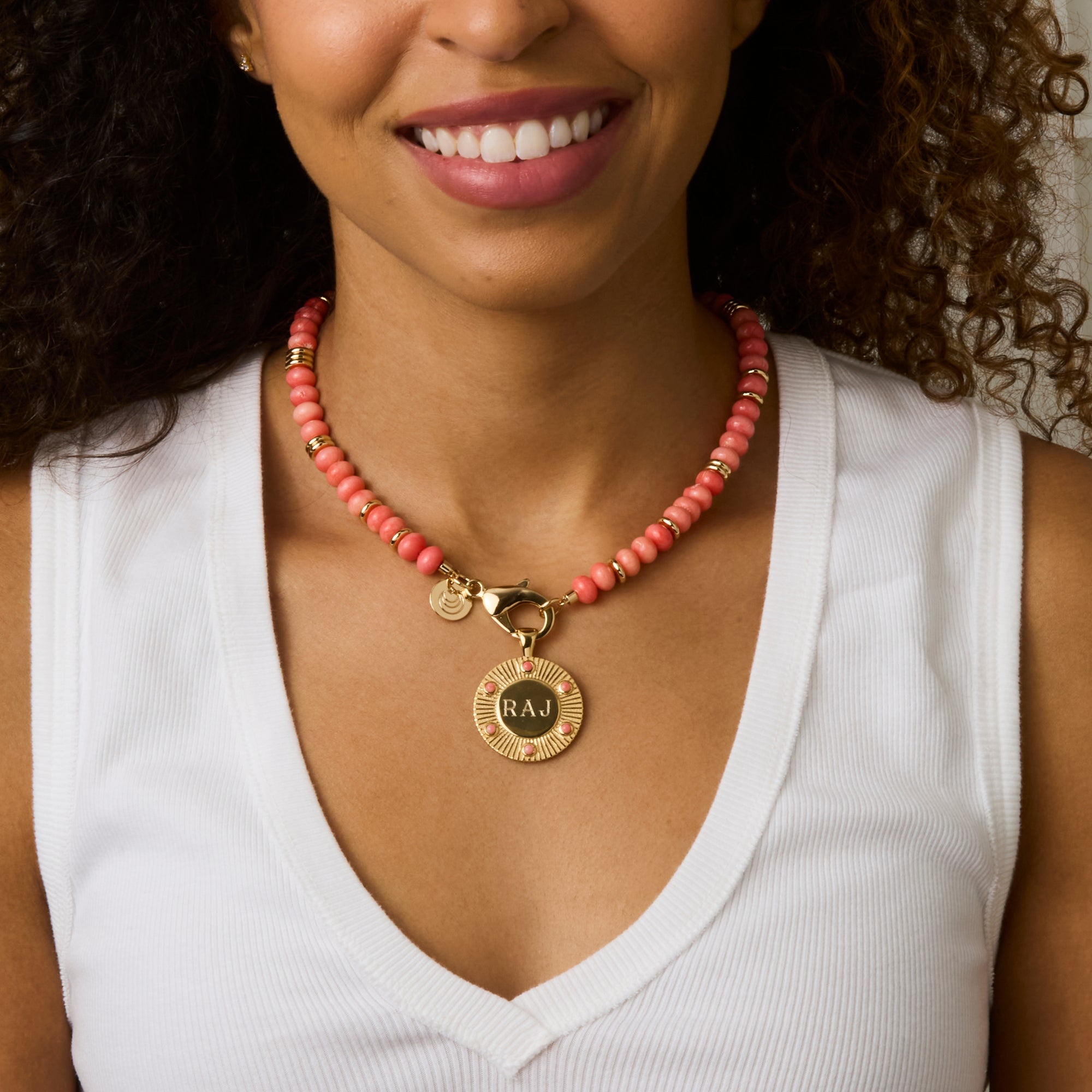 Model wearing the coral gumdrop beaded necklace with and engraved forever around the sun pendant in coral