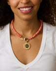 Model wearing the coral gumdrop beaded necklace with and engraved forever around the sun pendant in coral
