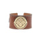Brown leather cuff with white stitching features gold love coin in the center