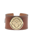 Brown leather cuff with white stitching features gold love coin in the center