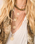 Blonde haired woman with white blouse, leopard vest, and wearing four gold pendant necklaces