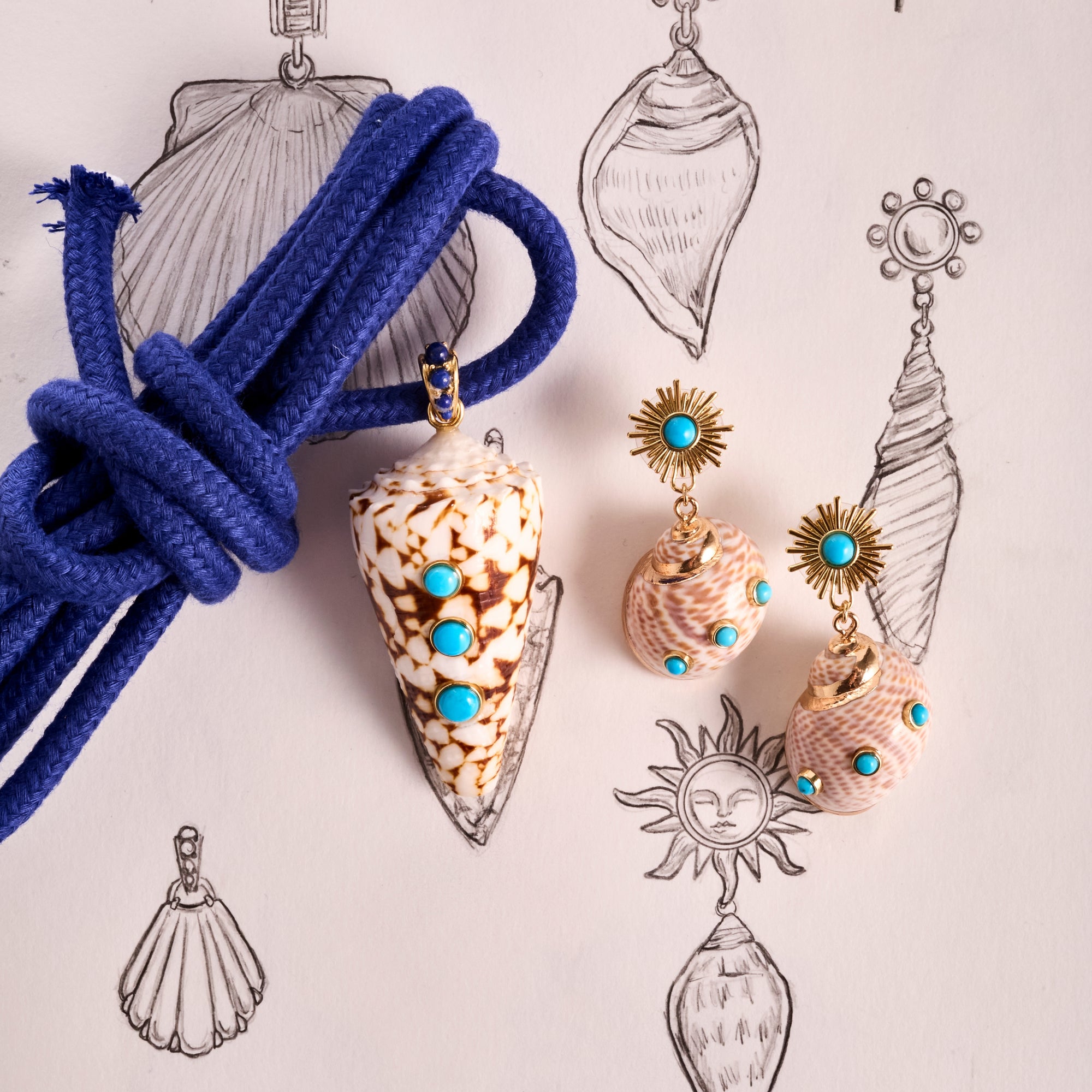 Stylized shot of the strong in the shallows shell pendant and strong soaking up the sun earrings. Shown with knotted blue rope and background of seashell drawings